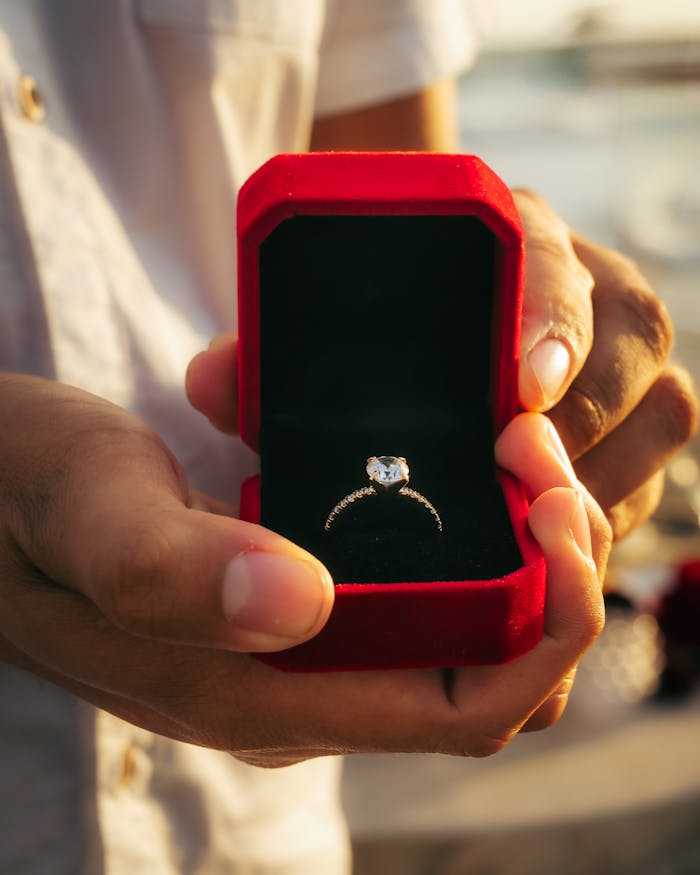 Close-up of a diamond engagement ring in a red velvet box held by a person, symbolizing love.
