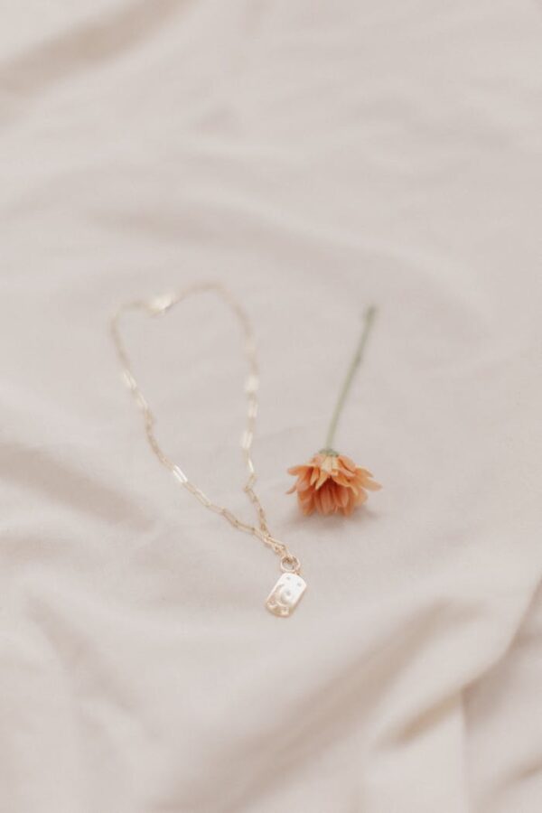 Close-up of gold necklace with pendant and orange flower on soft fabric, minimalist style.